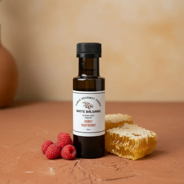 Honey Raspberry Dark Balsamic Vinegar bottle with raspberries and honeycomb on terracotta surface