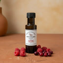 Raspberry Cranberry White Balsamic Vinegar bottle with fresh raspberries and cranberries on terracotta surface
